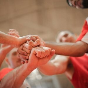 From below of crop multiethnic team of professional basketball players gathering and putting hands together while standing on playground before game